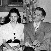 Old photo of a dapper, dark-haired man seated next to a dark-haired woman